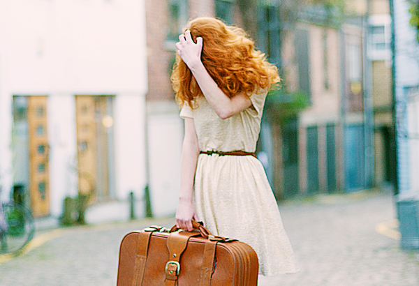 woman holding suitcase covering face