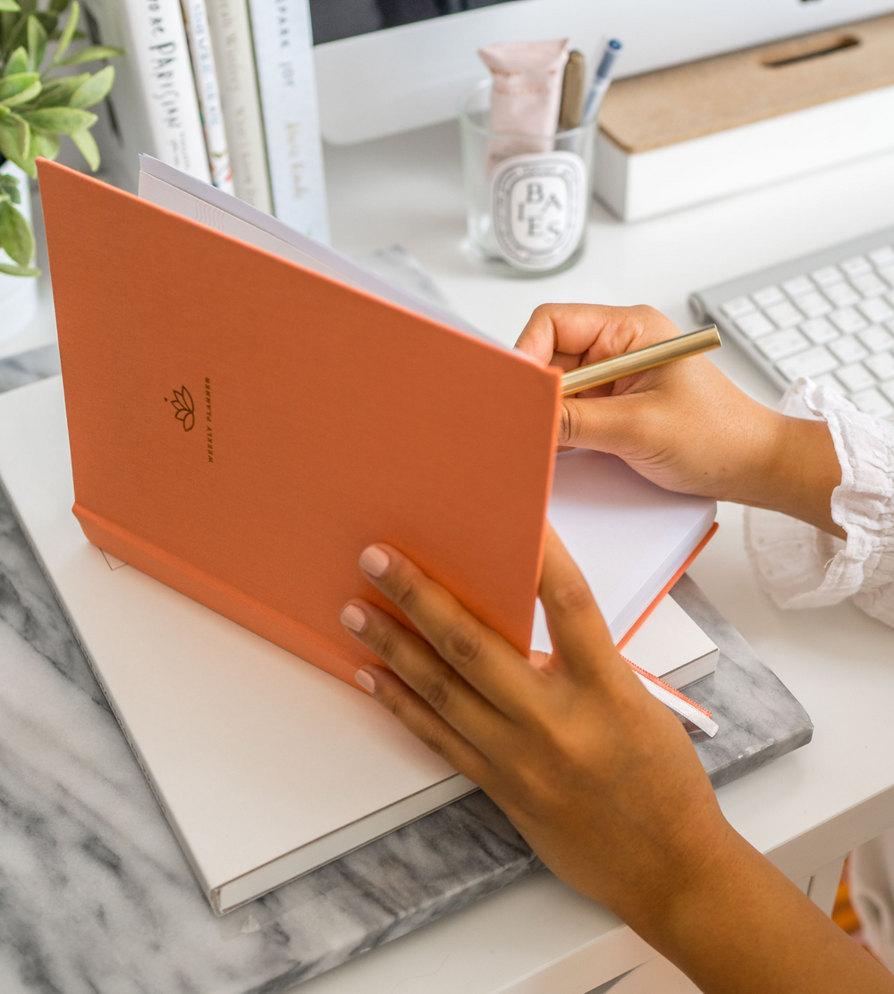 Picture of woman writing in coral undated planner