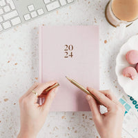 Woman holding the 2024 Weekly Ponderlily Planner in Blush Pink on desk