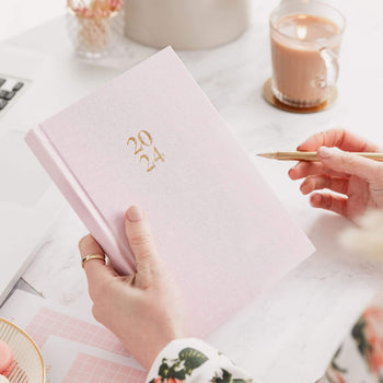 Woman holding the 2024 Weekly Ponderlily Planner cover in Blush Pink with pen