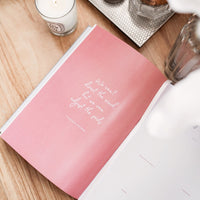 Ponderlily planner opened to inspirational quote page on desk, next to candles.